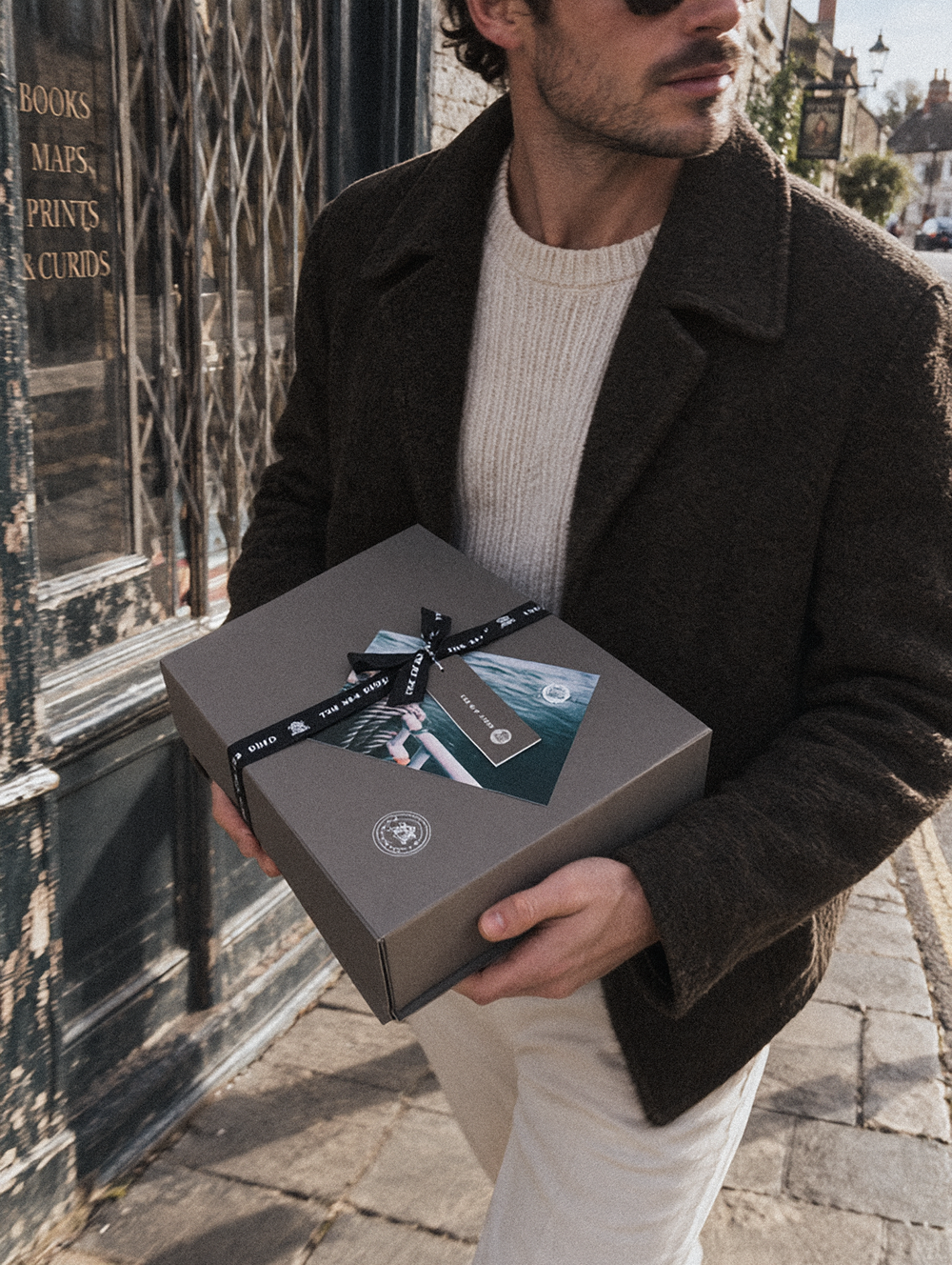 Man carrying a grey Sea Shed gift box tied with black branded ribbon past a bookshop