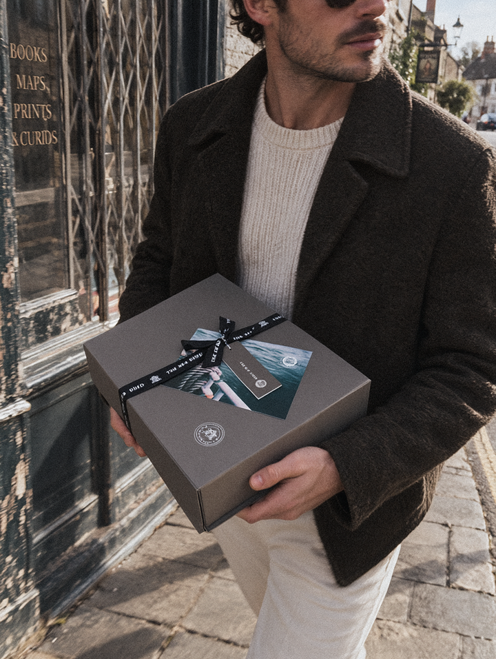 Man carrying a grey Sea Shed gift box tied with black branded ribbon past a bookshop